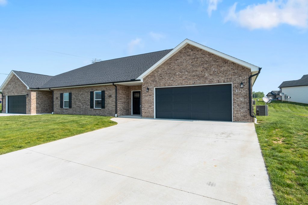 Modern brick duplex home with attached garage and concrete driveway in sunny weather.