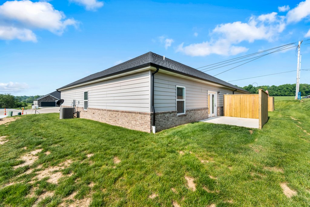 Single-story house with light gray siding, brick base, and fenced patio area in a grassy yard.