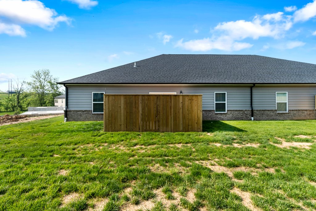 Backyard view of a grey house with a wooden fence and green lawn under a blue sky.