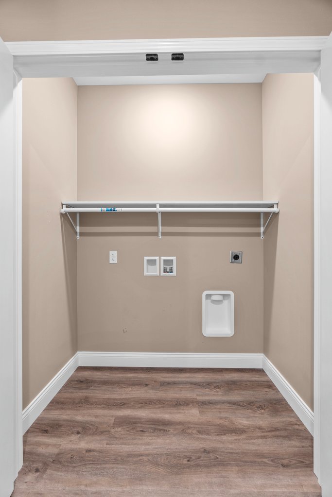 Empty laundry room with white shelf, outlets, dryer vent, and floor.