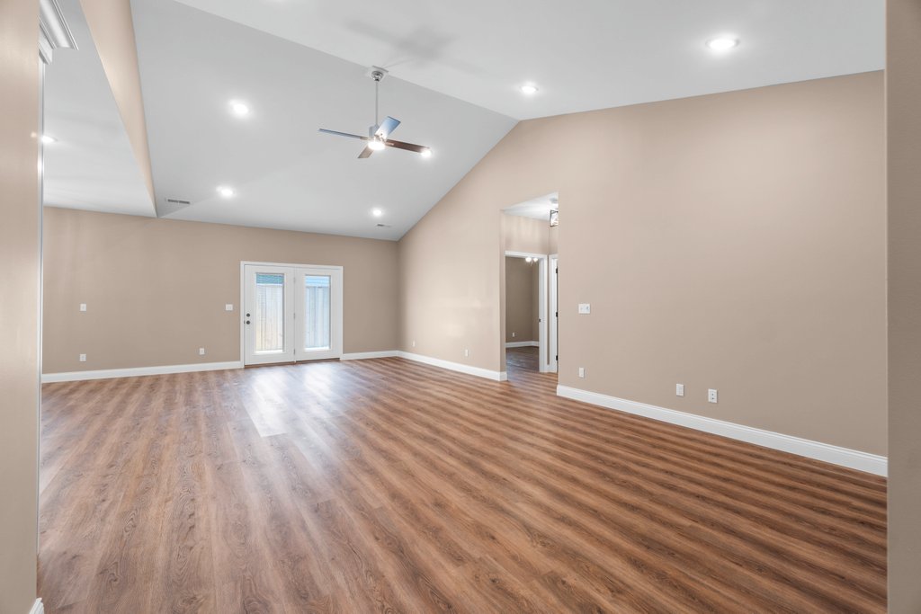Spacious living room with vaulted ceiling, fan, and double doors.