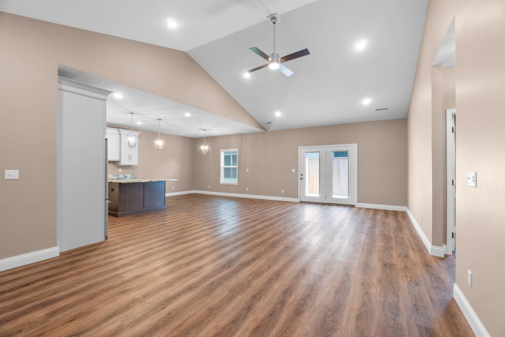 Open-concept living and kitchen area with vaulted ceiling, wood floors, and double doors.