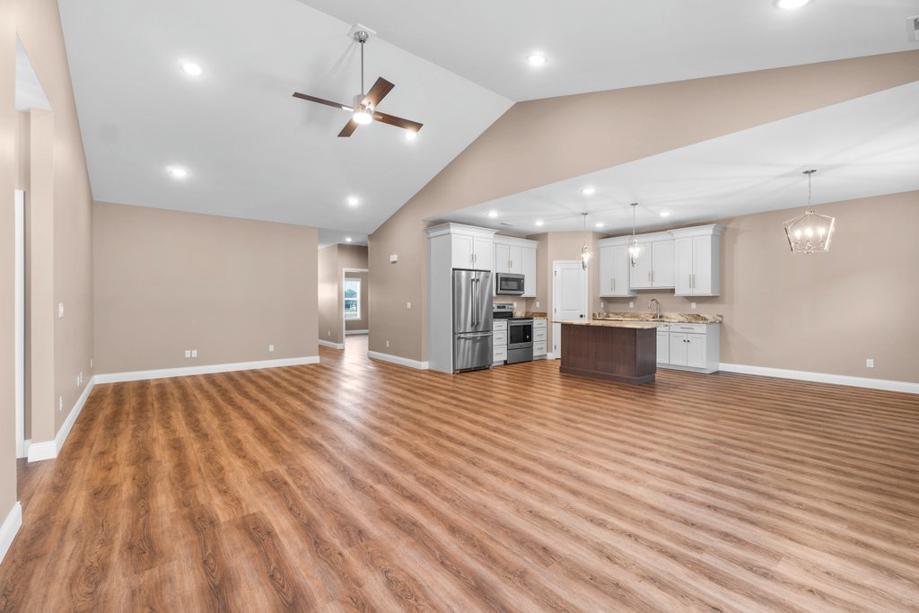 Modern open-plan living area with vaulted ceiling, kitchen island, and wood-look flooring.