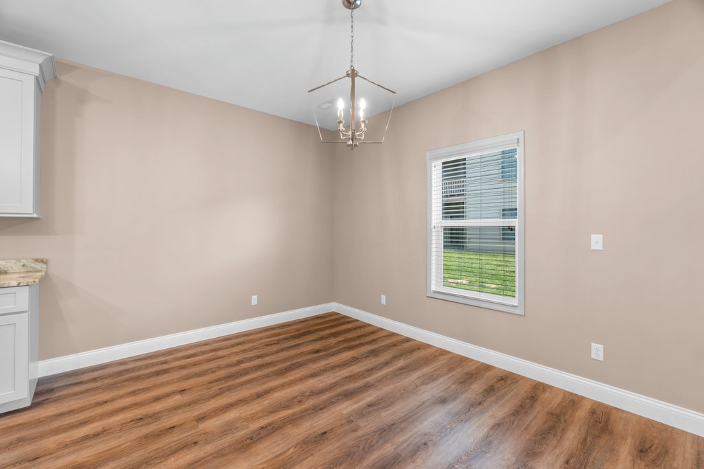Empty dining room with tan walls, wood floors, and a modern chandelier.