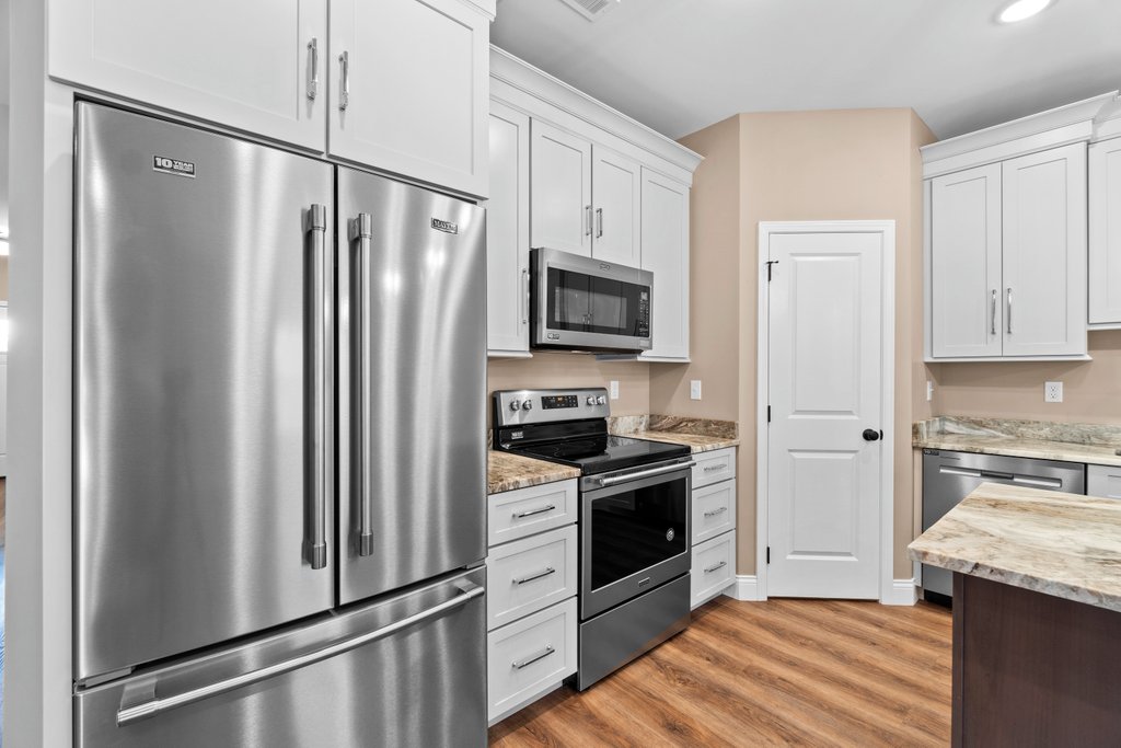 Stainless steel refrigerator and modern kitchen with white cabinets, oven, and microwave.