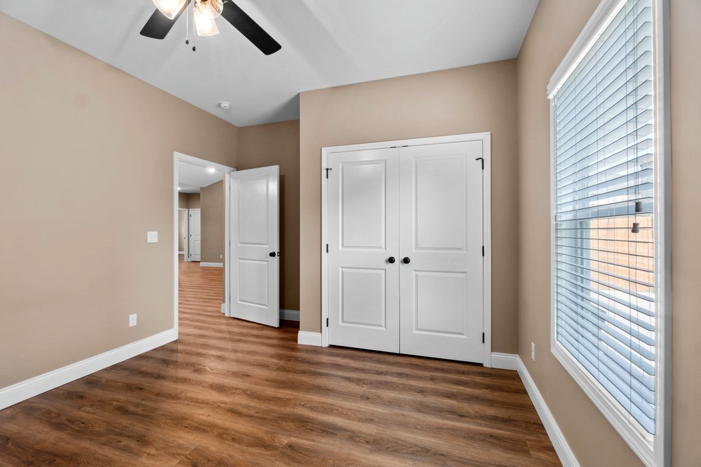 Interior view of a bedroom with light brown walls, wood floors, and white doors, including a closet.