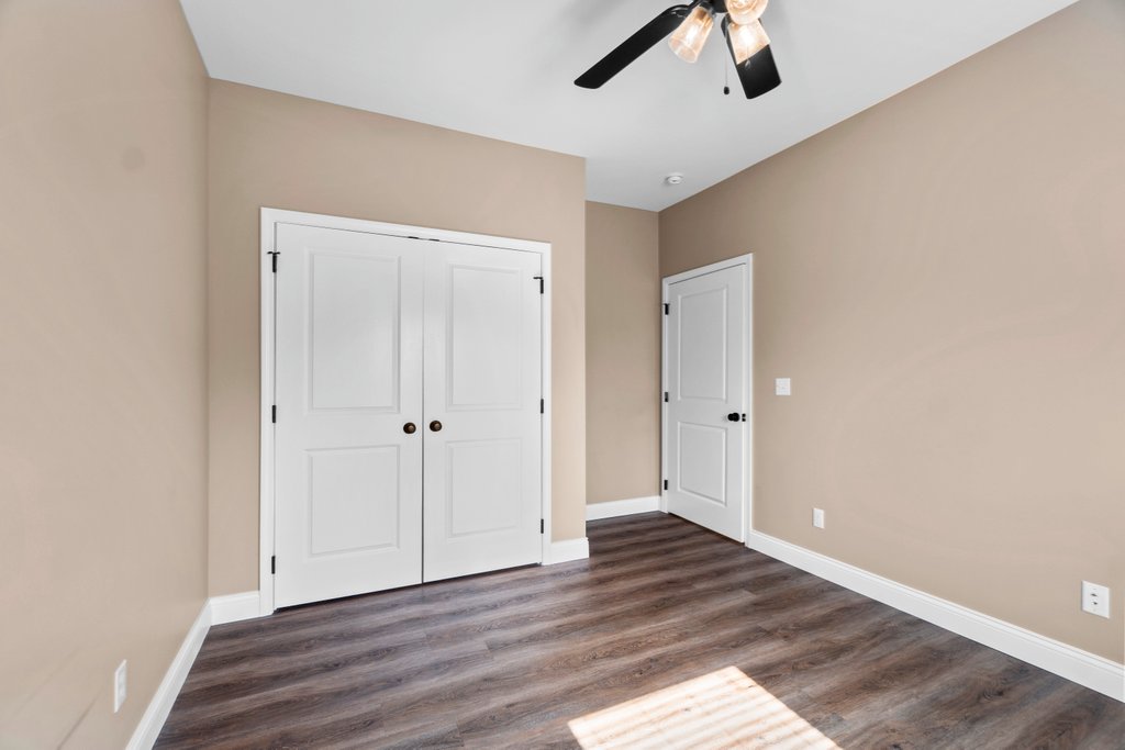 Modern bedroom with beige walls, white double doors, and dark wood laminate flooring.