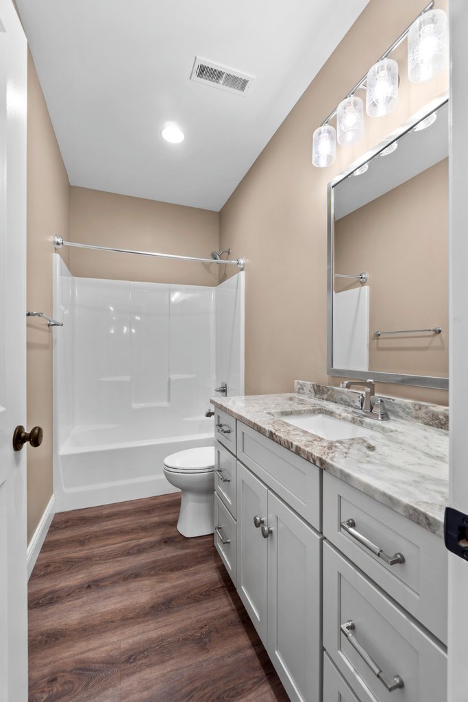 Modern bathroom with white tub, toilet, vanity, and marble countertop.