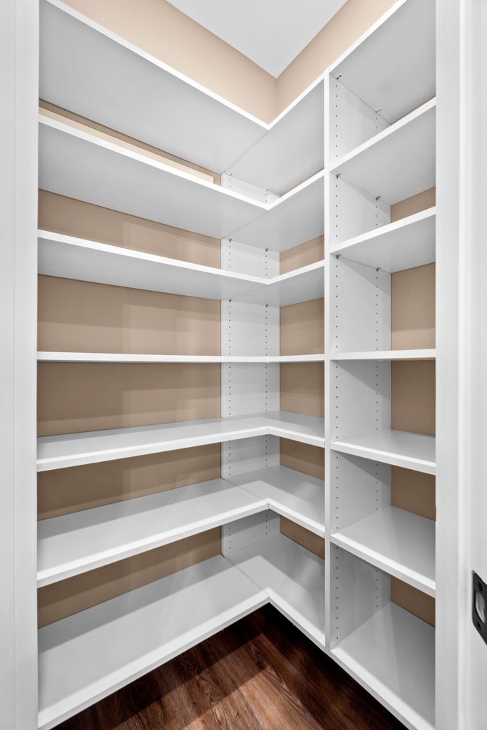 Empty white corner pantry shelves with tan walls and dark wood floor.